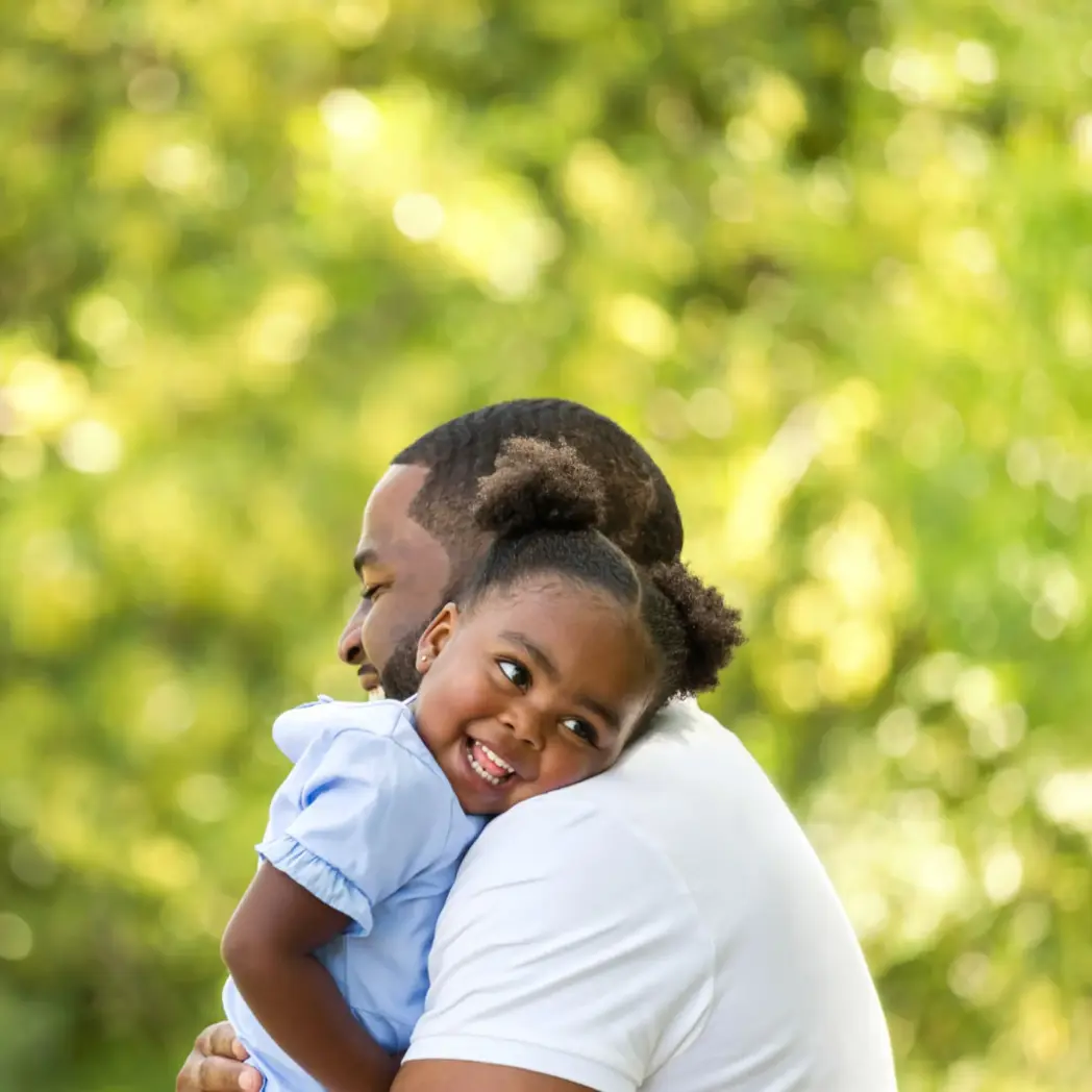 A black man holds his young daughter outside