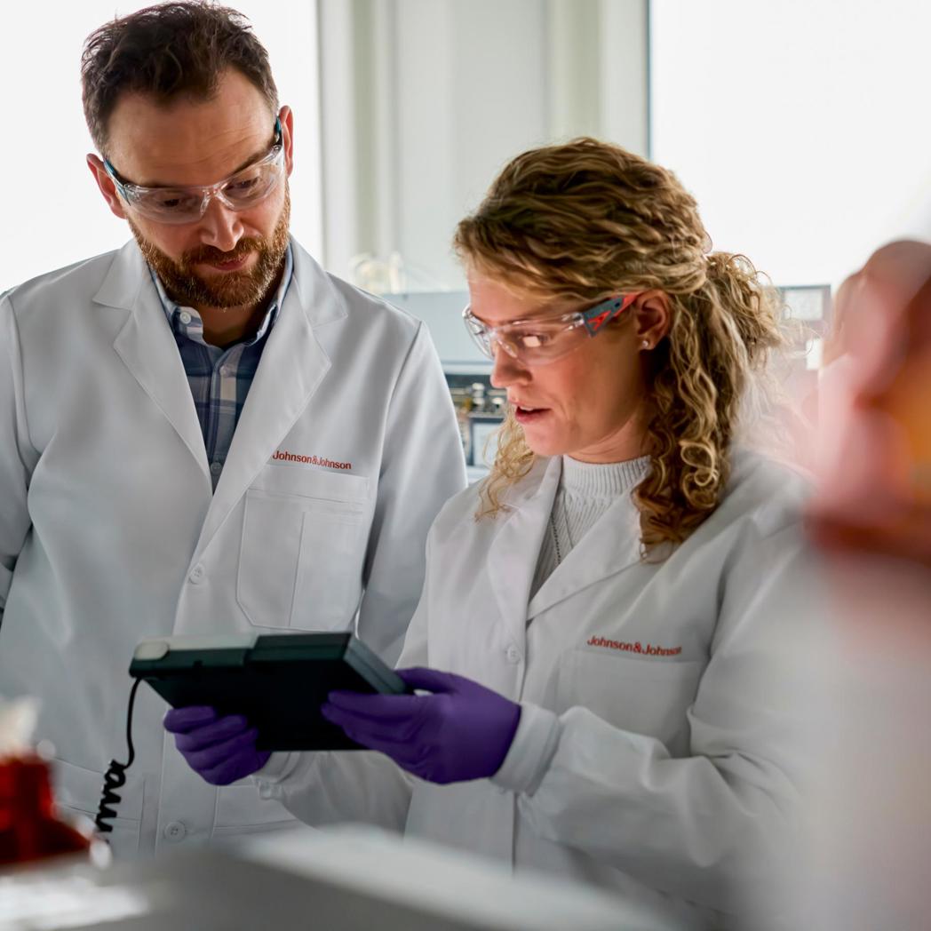 A man and woman in white lab coats look at a tablet