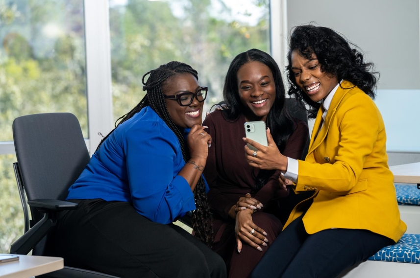 Three women enjoying a laugh while looking at a phone