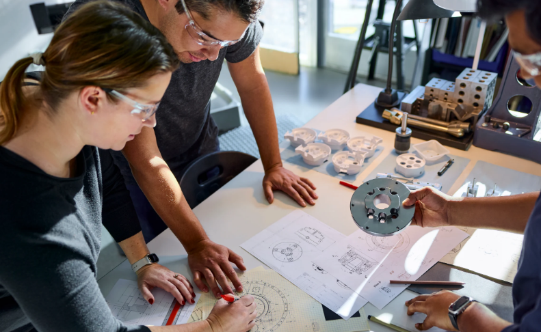 Colleagues collaborate around a desk with blueprints and technical diagrams