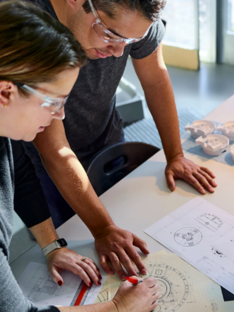 Colleagues collaborate around a desk with blueprints and technical diagrams