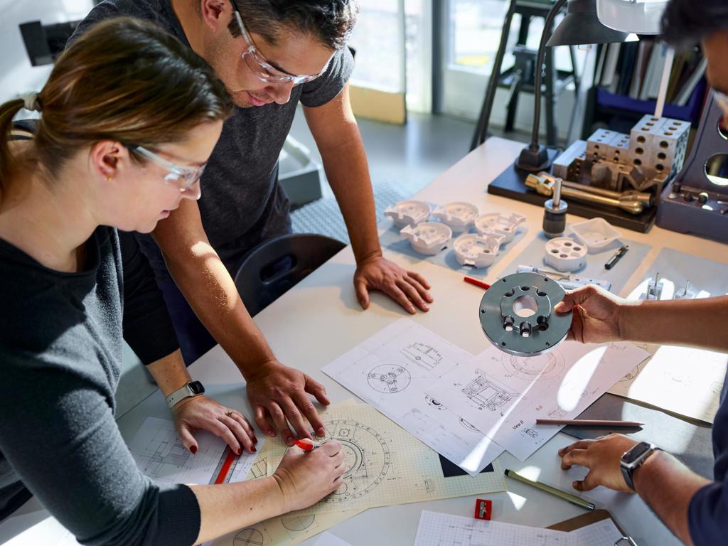 A top-down view of three people collaborating on medtech schematics and looking at device components.