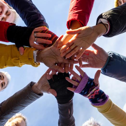 People standing in a circle clasping hands in unity. The picture is shot from below looking up at the connected hands.