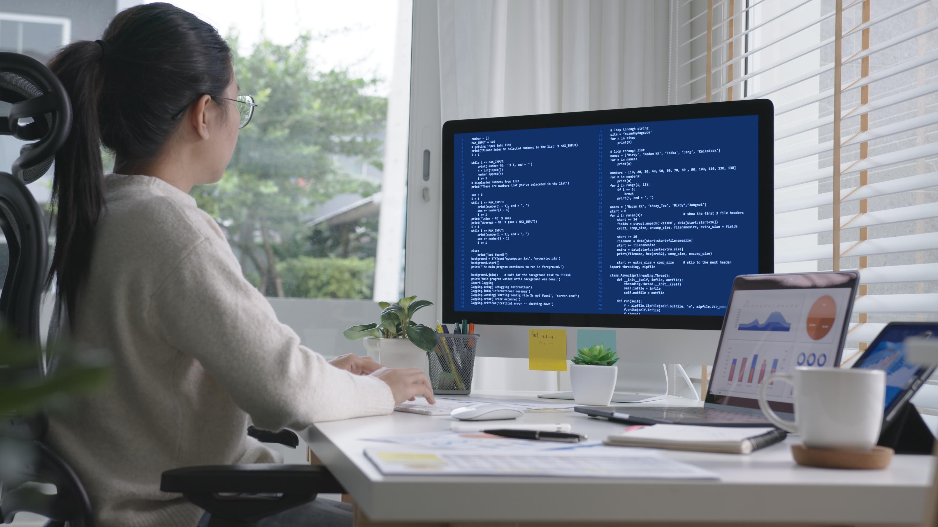 Young woman sits in front of a computer working on code