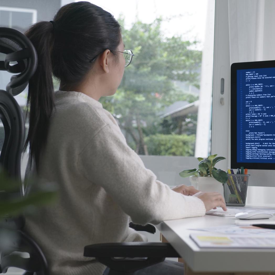 Young woman sits in front of a computer working on code