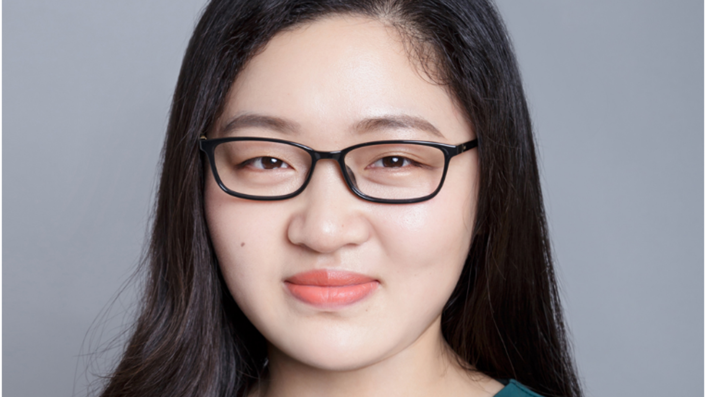 A headshot of an Asian woman wearing a long-sleeved teal top and glasses