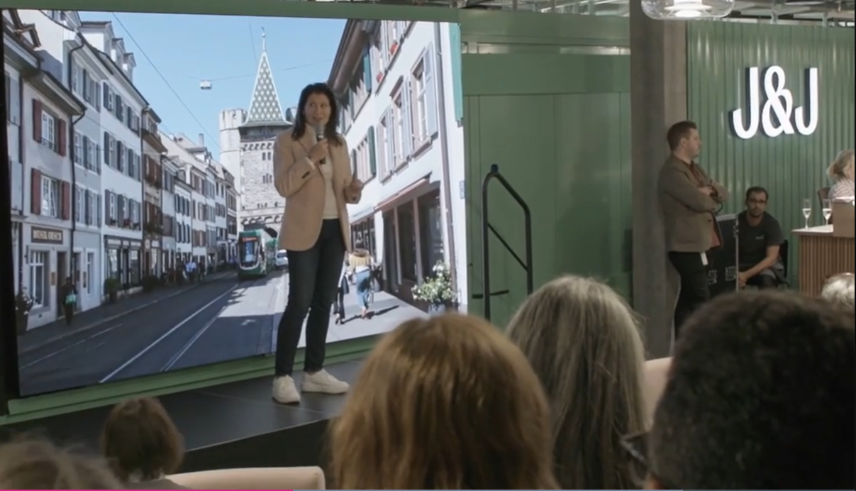 A woman standing on a stage in a J&J conference rom speaking to people in the room