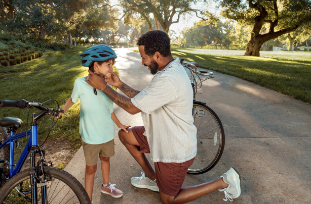 Father applies bicycle helmet to son