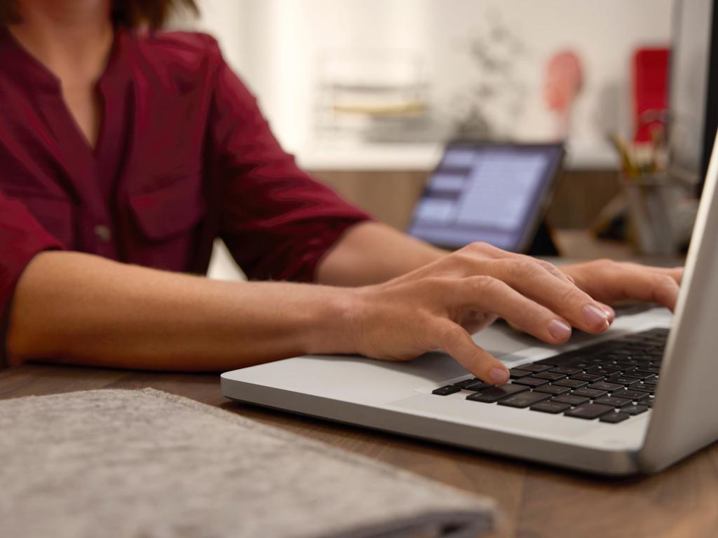 A woman types on a laptop on a desk in an office