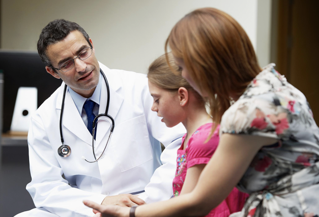 A physician speaking compassionately with a young girl and her mother
