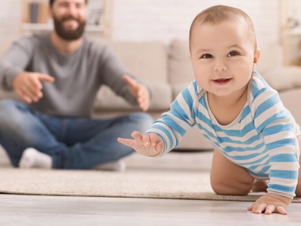 Man sitting on a floor watching a baby crawl