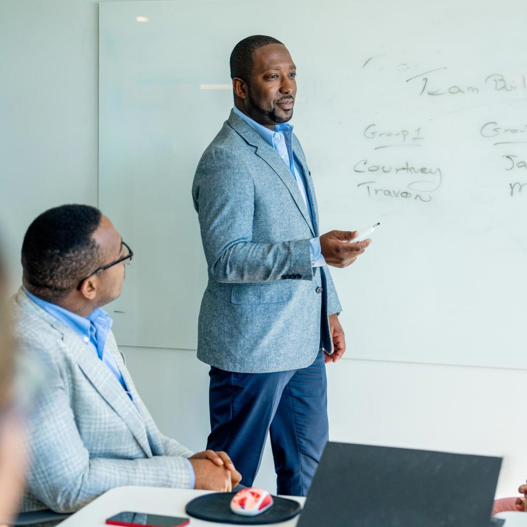 A man stands at a white board in an office leading a meeting