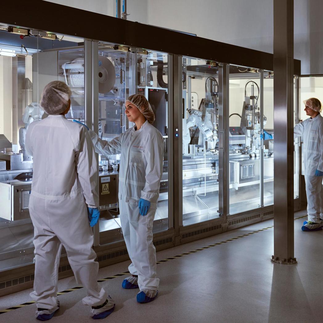 A pharmaceutical packaging area where two operations supervisors are standing in front of an automated packaging line,