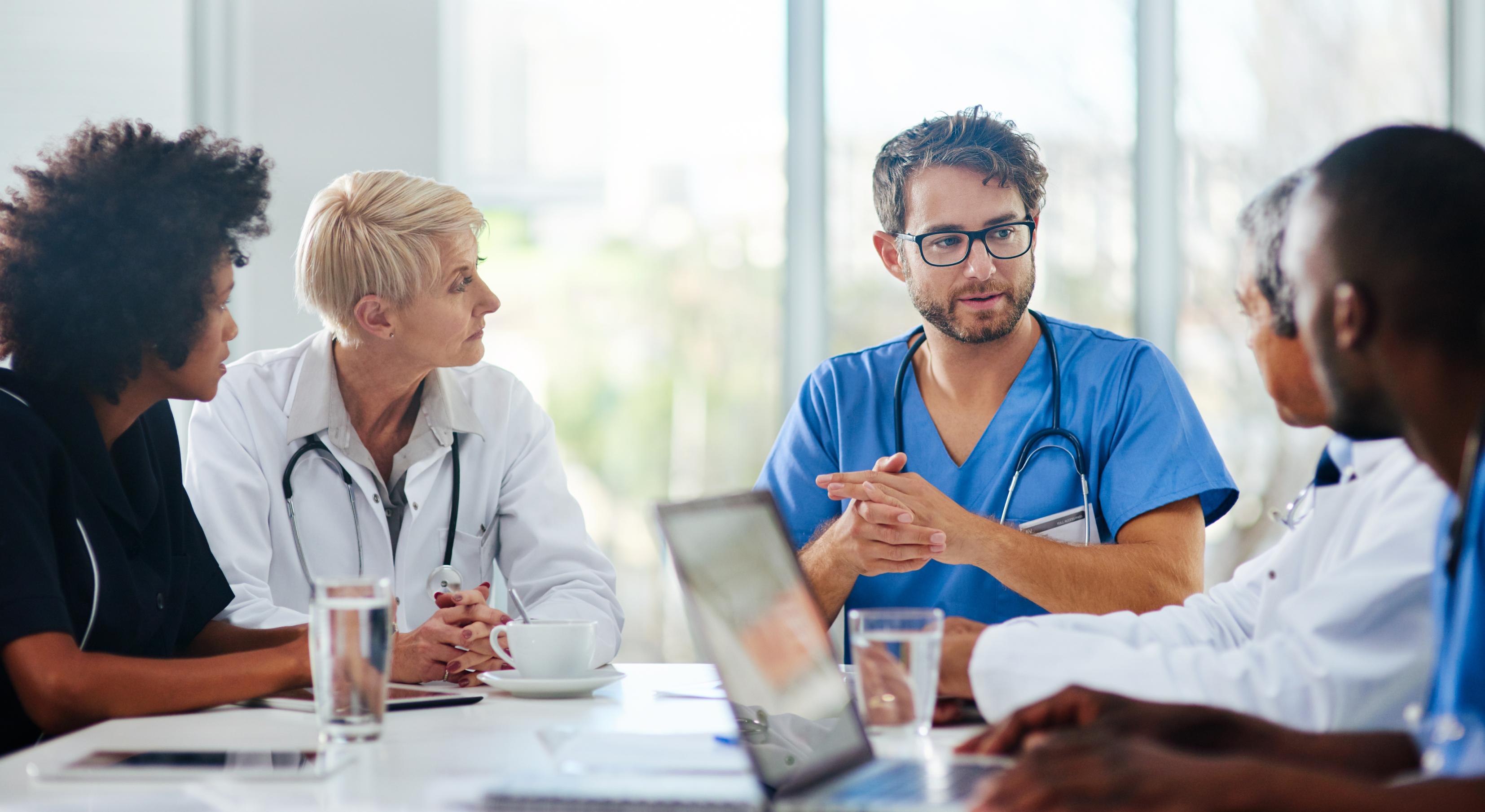 Healthcare professionals sit around a work table with windows in the background