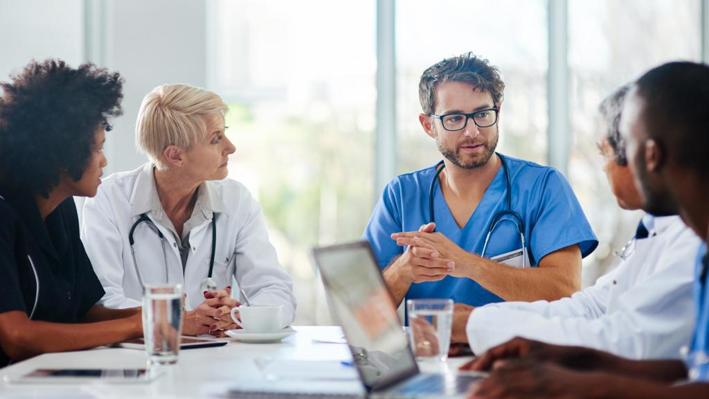 Healthcare professionals sit around a work table with windows in the background