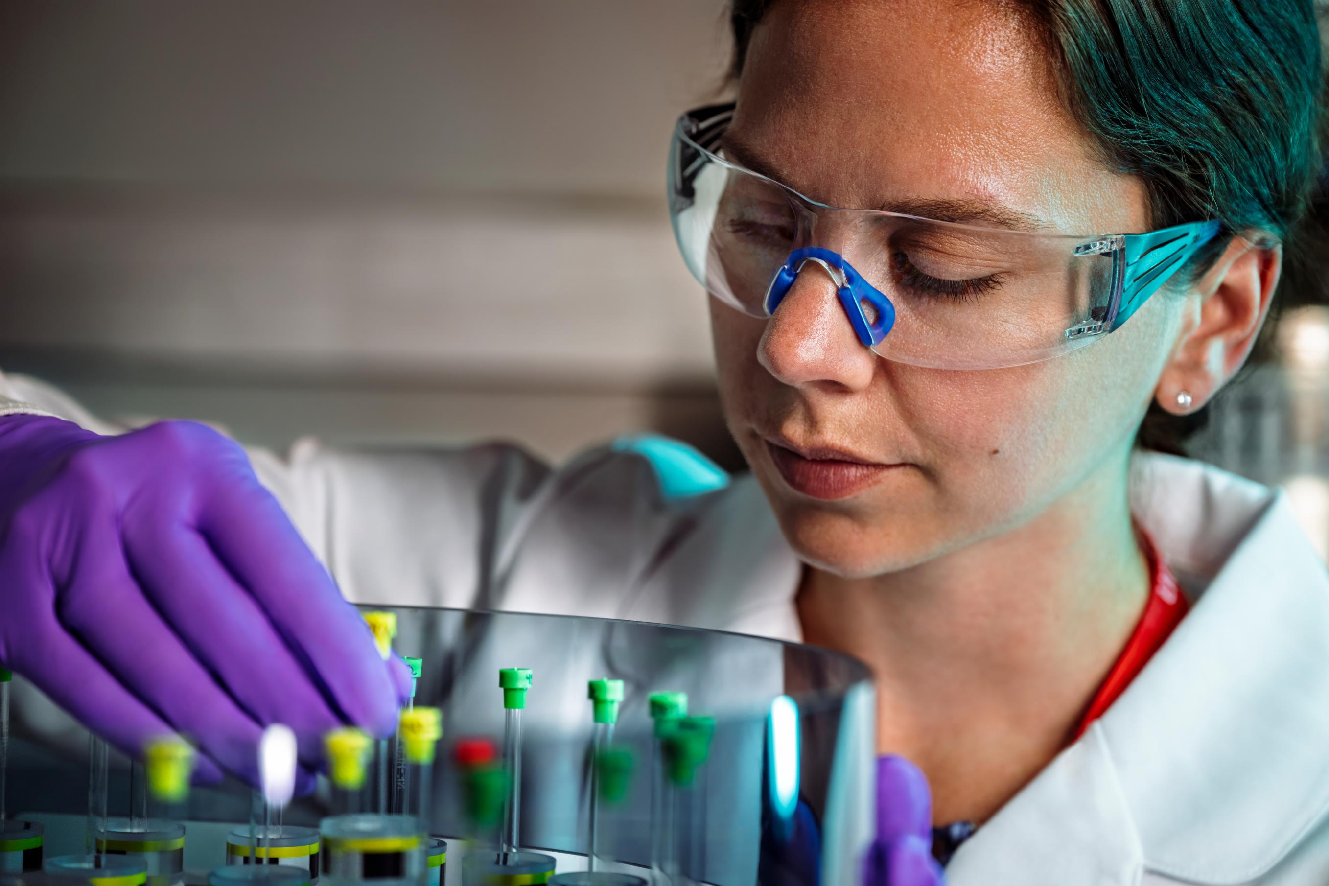 A woman in a lab coat and safety goggles organizes samples
