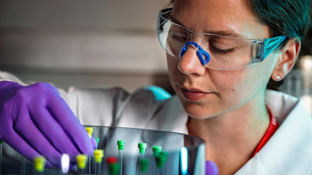A woman in a lab coat and safety goggles organizes samples